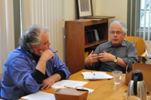 Two professors sit at an office table discussing something.