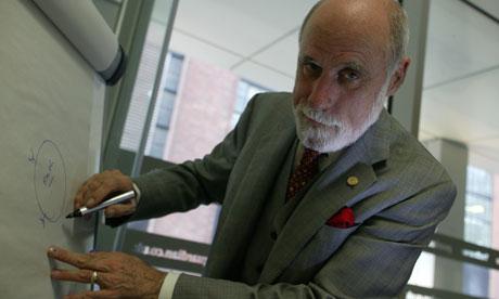 Image of Vint Cerf cracking a sly smile to the camera as he writes on the board.