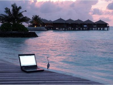 Photo of a laptop sitting on the beach at sunset.