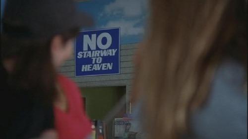 Between two blurred outlines of passersby, a sign reads "No stairway to heaven."