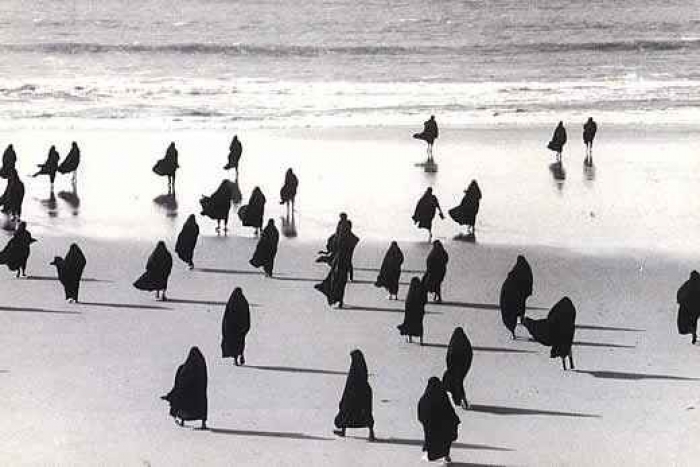Photo of women in black burqas on the beach, shot so that they resemble birds.