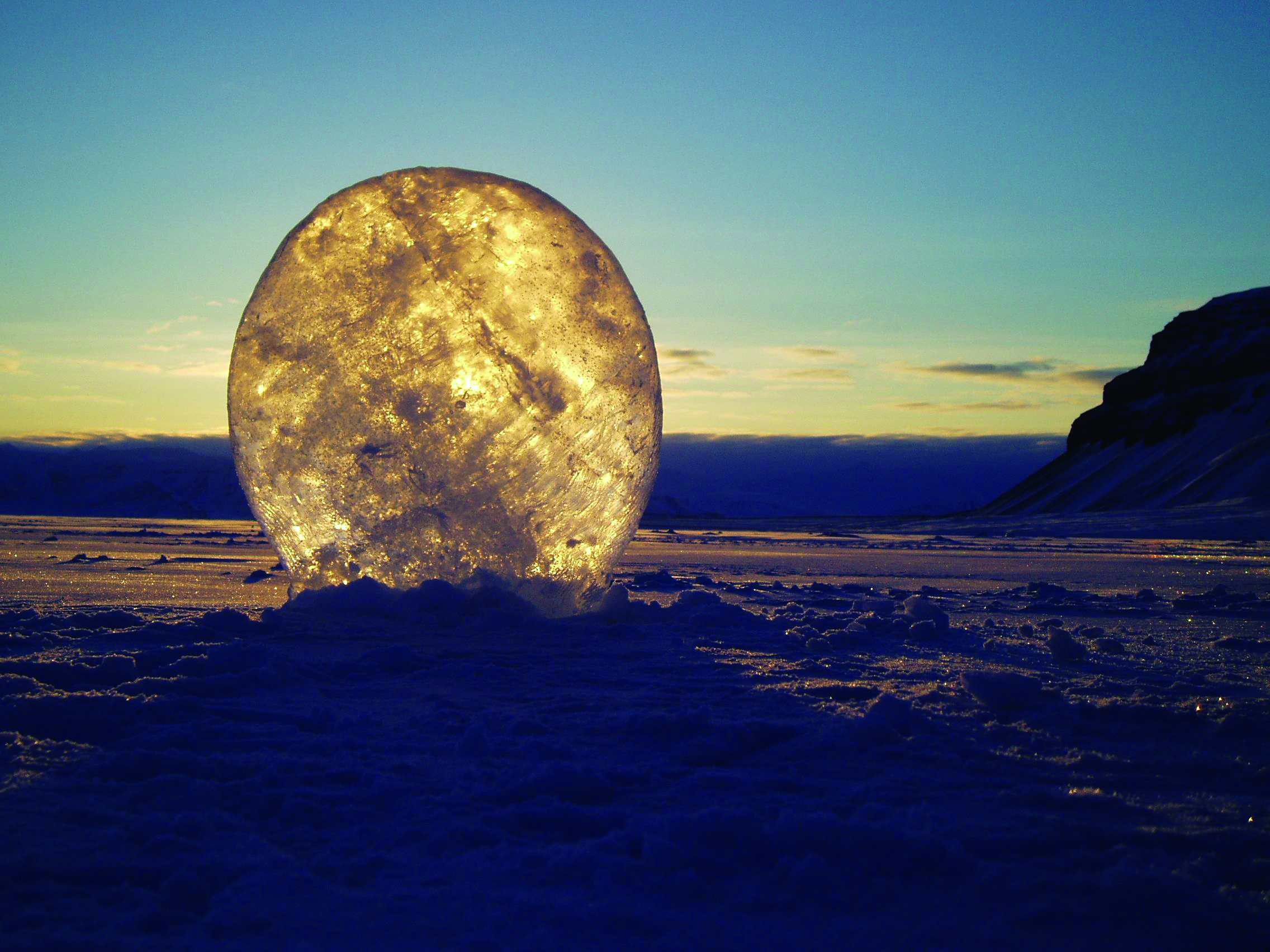 An artistic photo of a tall, thin circle of icy snow standing in front of the sun, appearing to glow like the moon.