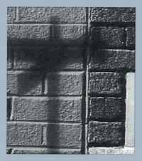 Black and white photo of the shadow of a street sign against a brick wall.