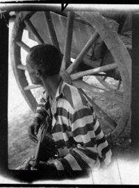 Photo of an African man sitting playing a stringed instrument, his face turned away from the camera.