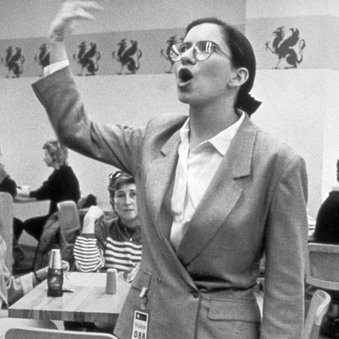 Black and White Photo of Standing Woman Speaking in a Cafeteria