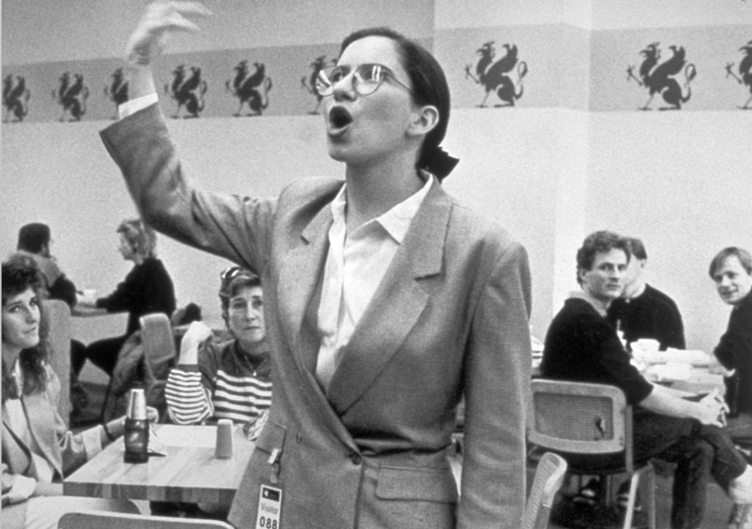 Black and White Photo of Standing Woman Speaking in a Cafeteria